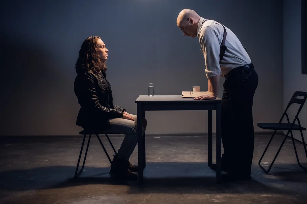 A male detective interrogating a woman in the interrogation room