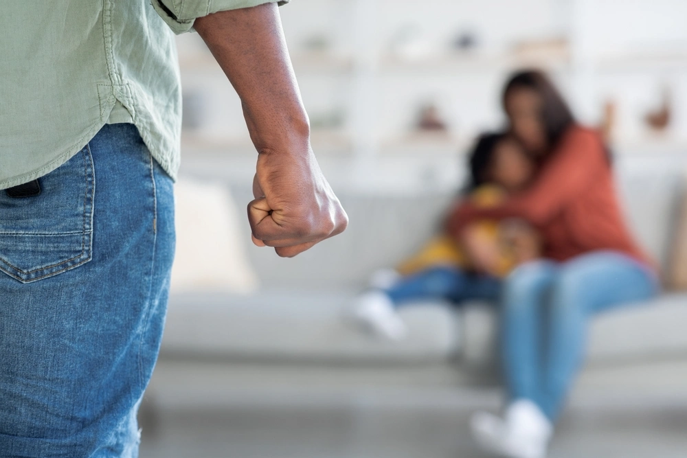 Man threatening woman and child with raised fist, focus on the hand.