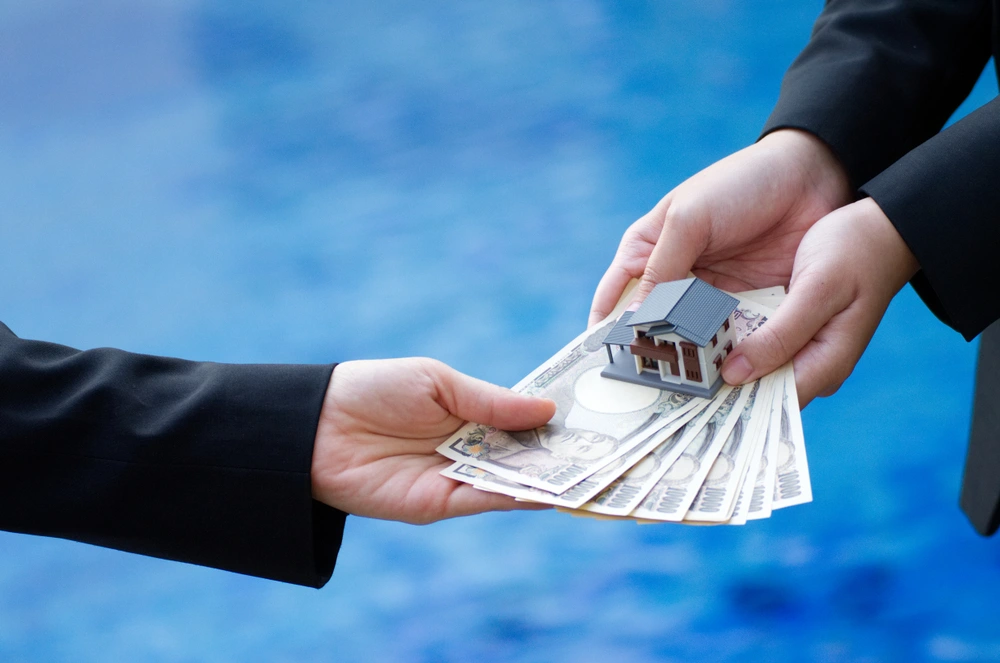 Hand holding banknotes of the Japanese yen and house model.