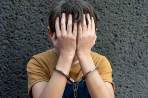A 10-year-old boy in handcuffs sits on a gray background.